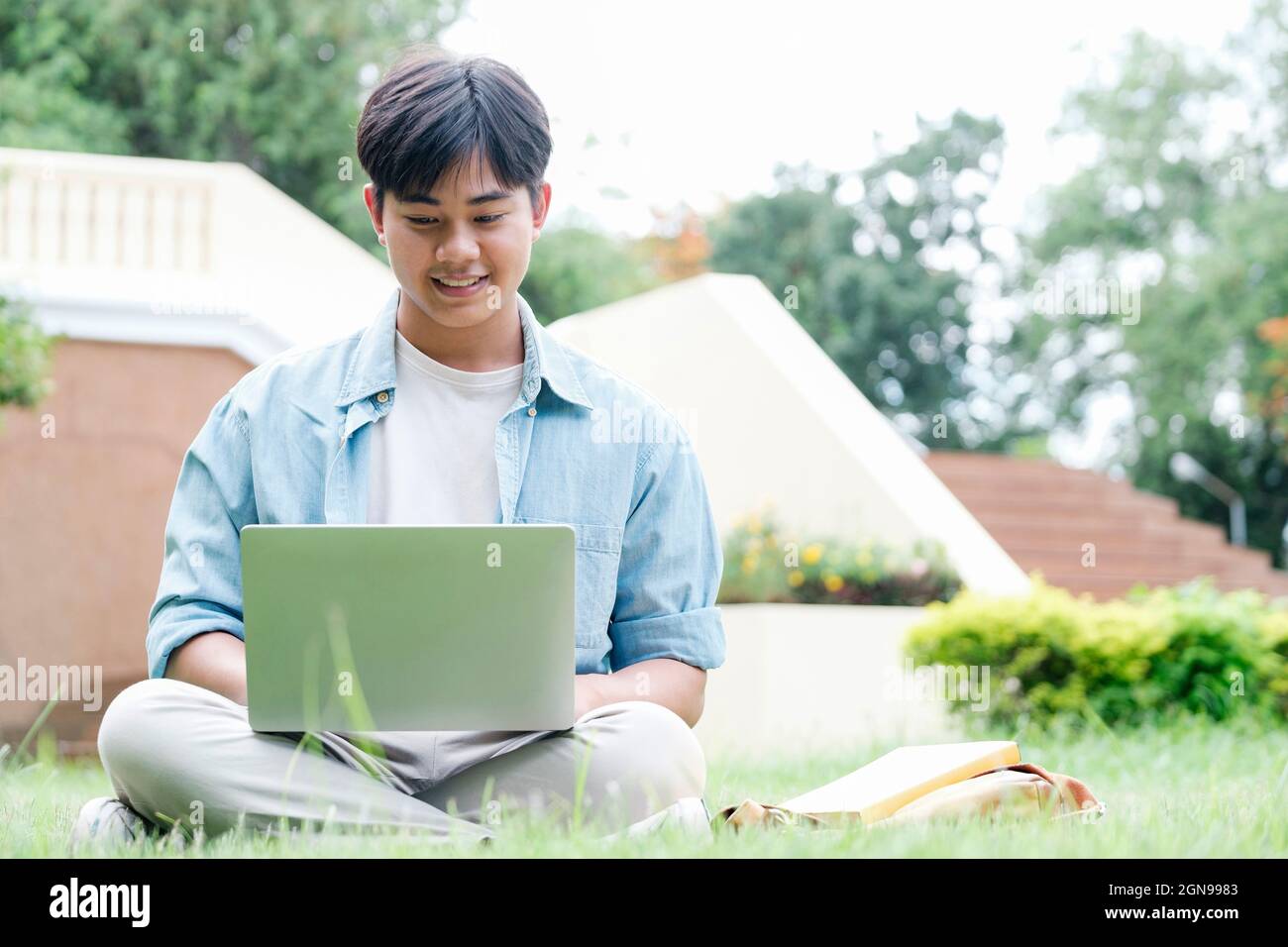 Collage student using laptop sitting at the campus yard, online study concept. Stock Photo