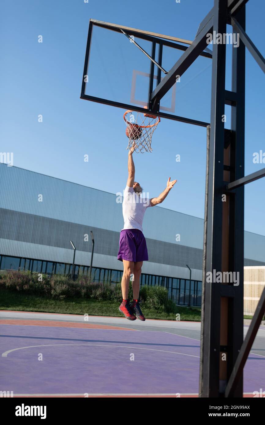 Athlete jumping and shooting ball into basket while playing streetball on court Stock Photo
