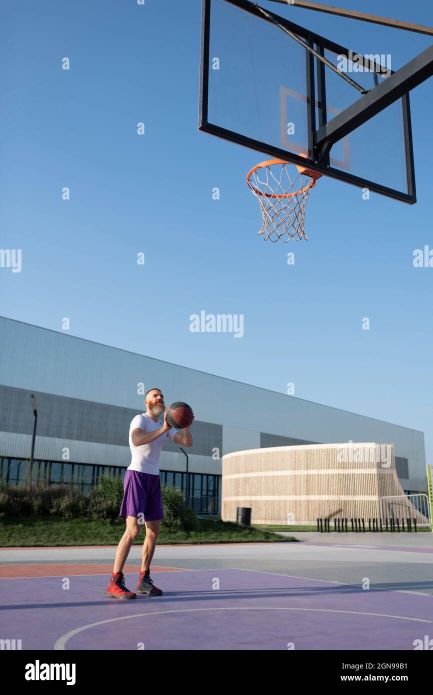 Male athlete preparing to score into basket on streetball court on sunny summer day Stock Photo