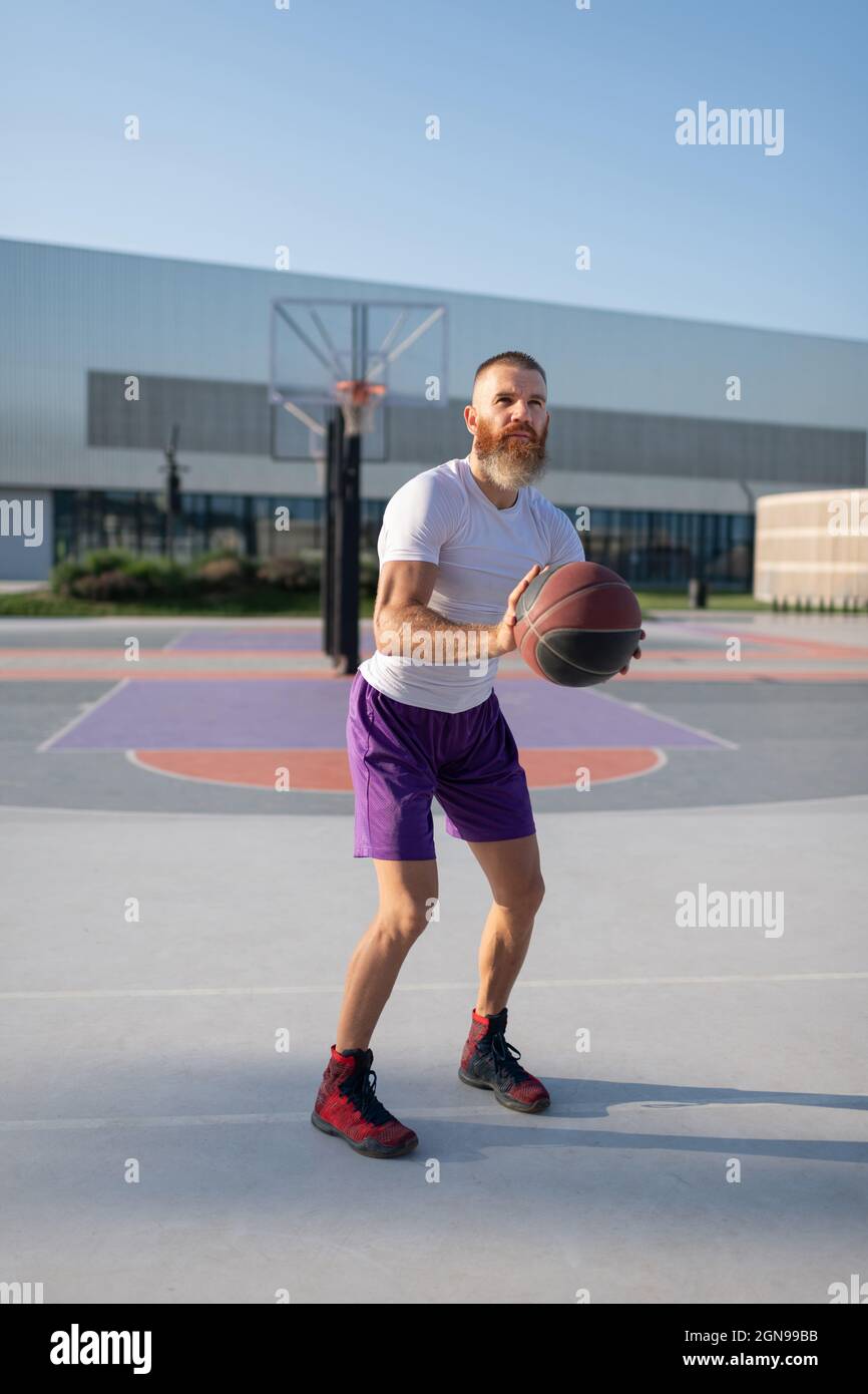 Bearded man in sportswear preparing to shoot ball during basketball training Stock Photo