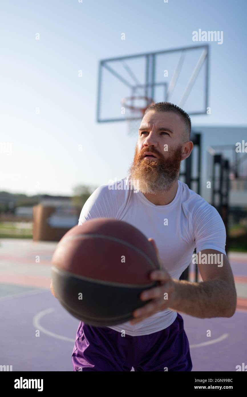Bearded sportsman preparing to throw ball while playing basketball in summer Stock Photo