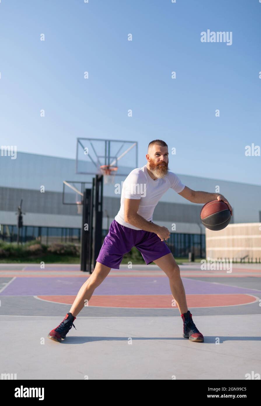 Bearded sportsman practicing to dribble ball during streetball training on court Stock Photo