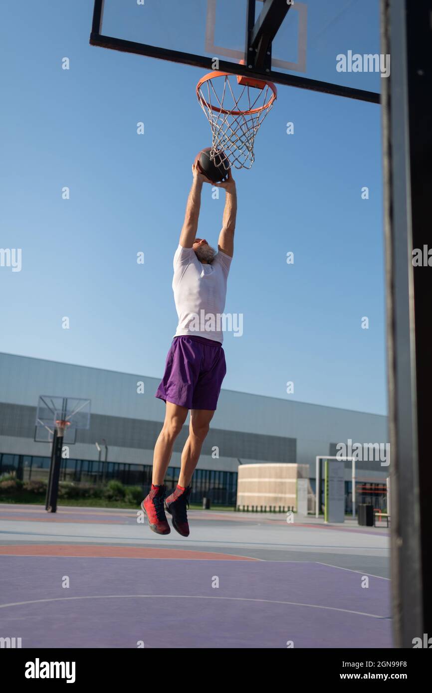 Male athlete leaping and throwing ball into hoop during streetball training Stock Photo