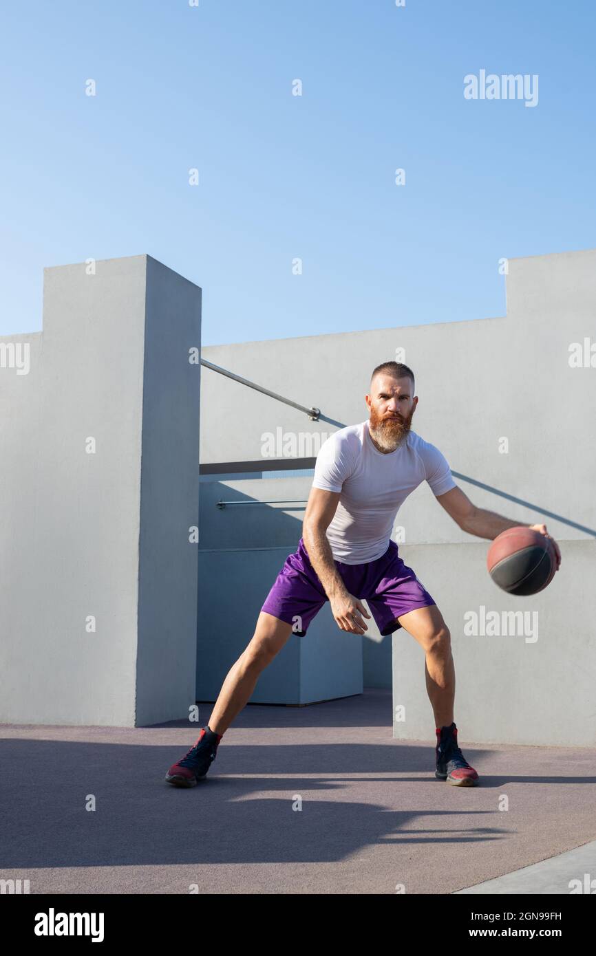 Skilled sportsman in activewear practicing dribbling exercise with basketball ball during outdoor training Stock Photo