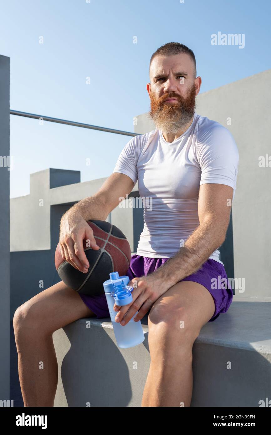 Confident male athlete in sportswear holding bottle of cold water and looking at camera Stock Photo