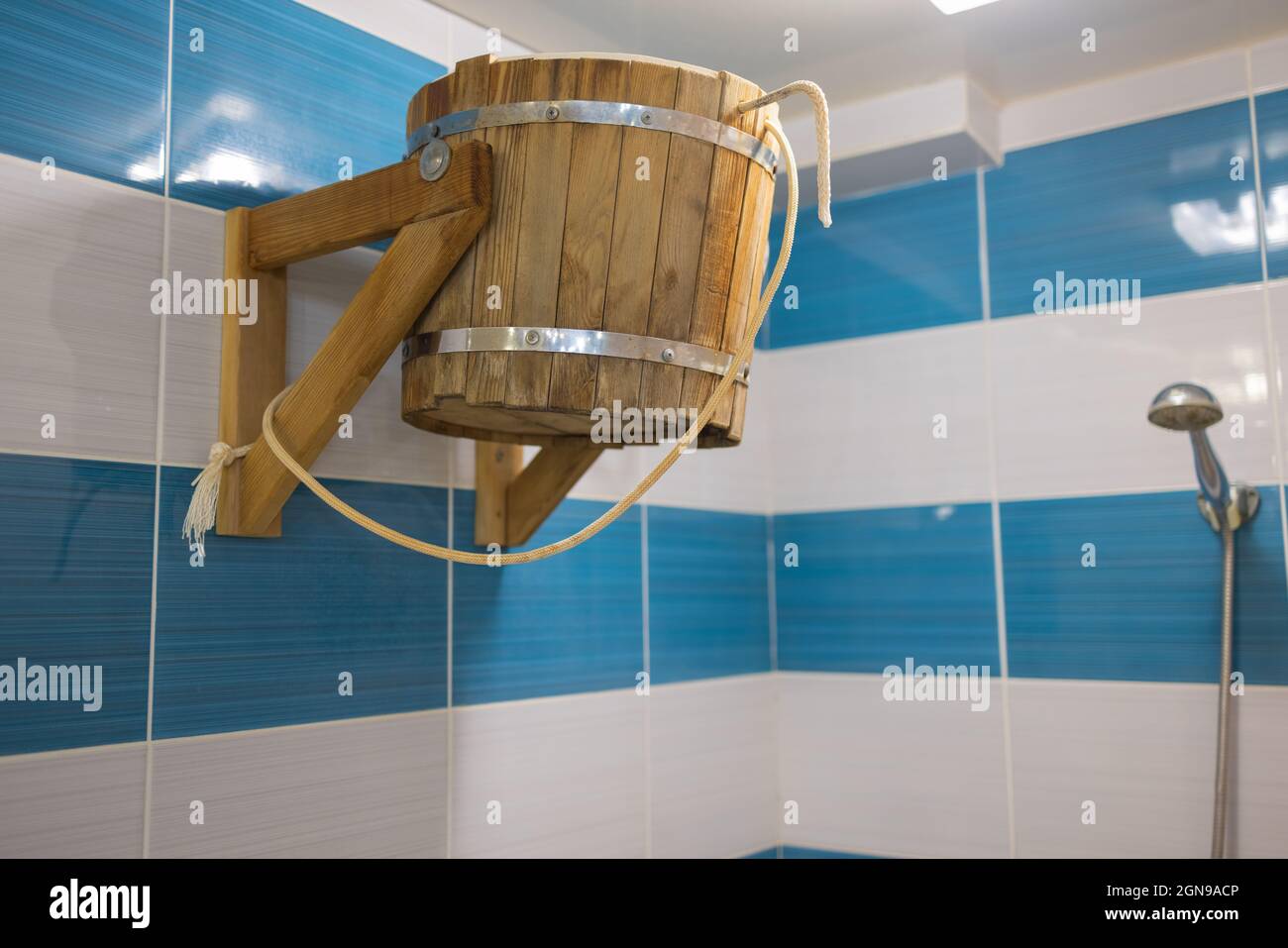 Wooden tipping bucket hangs on stone wall in sauna Stock Photo