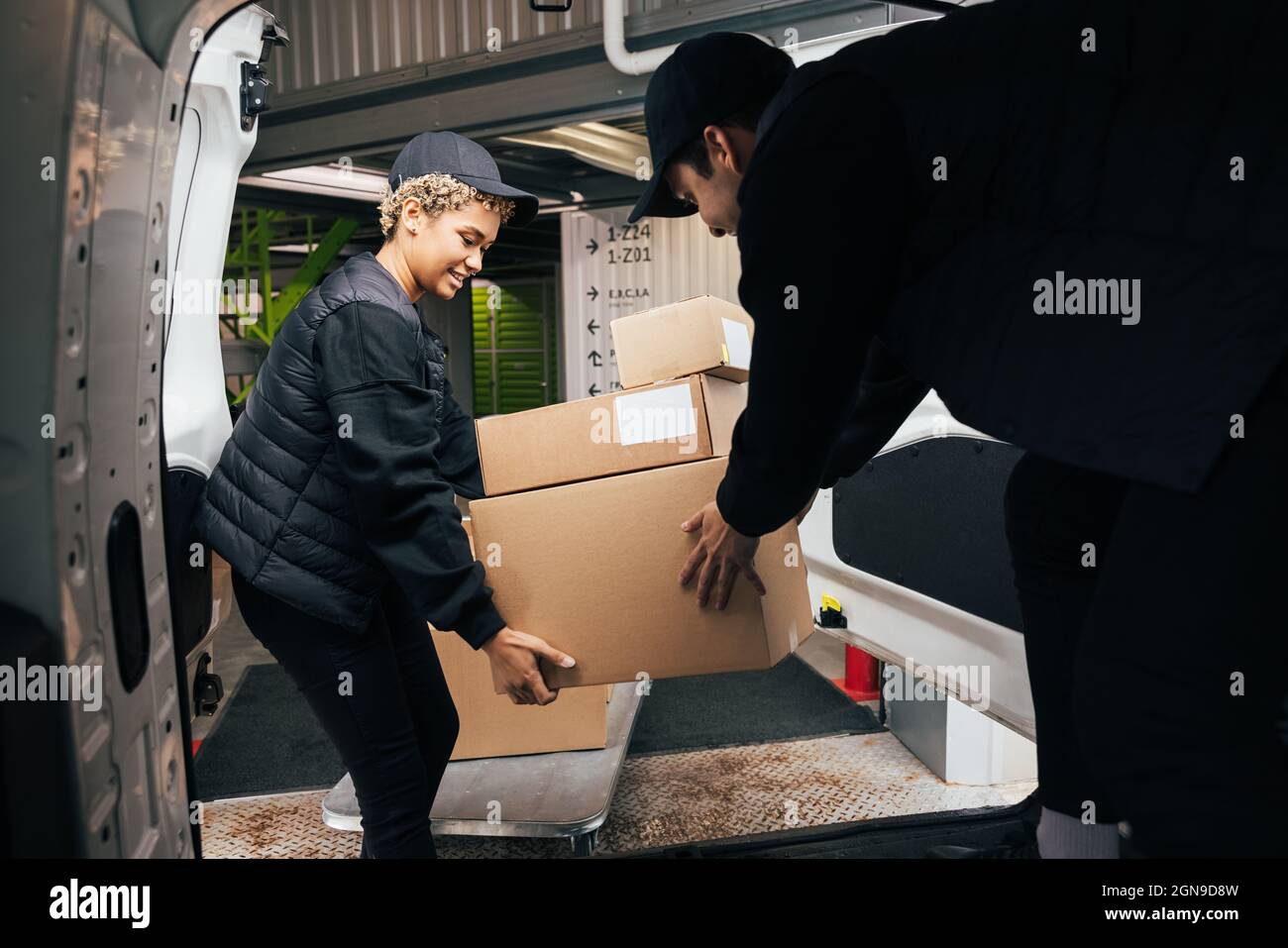 Two couriers stack cardboard boxes in a delivery van. Coworkers pick up