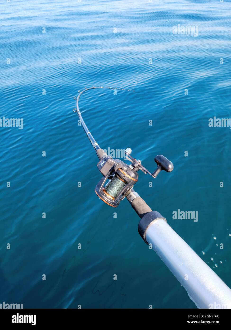 Fishing pole with reel in blue lake water Stock Photo - Alamy