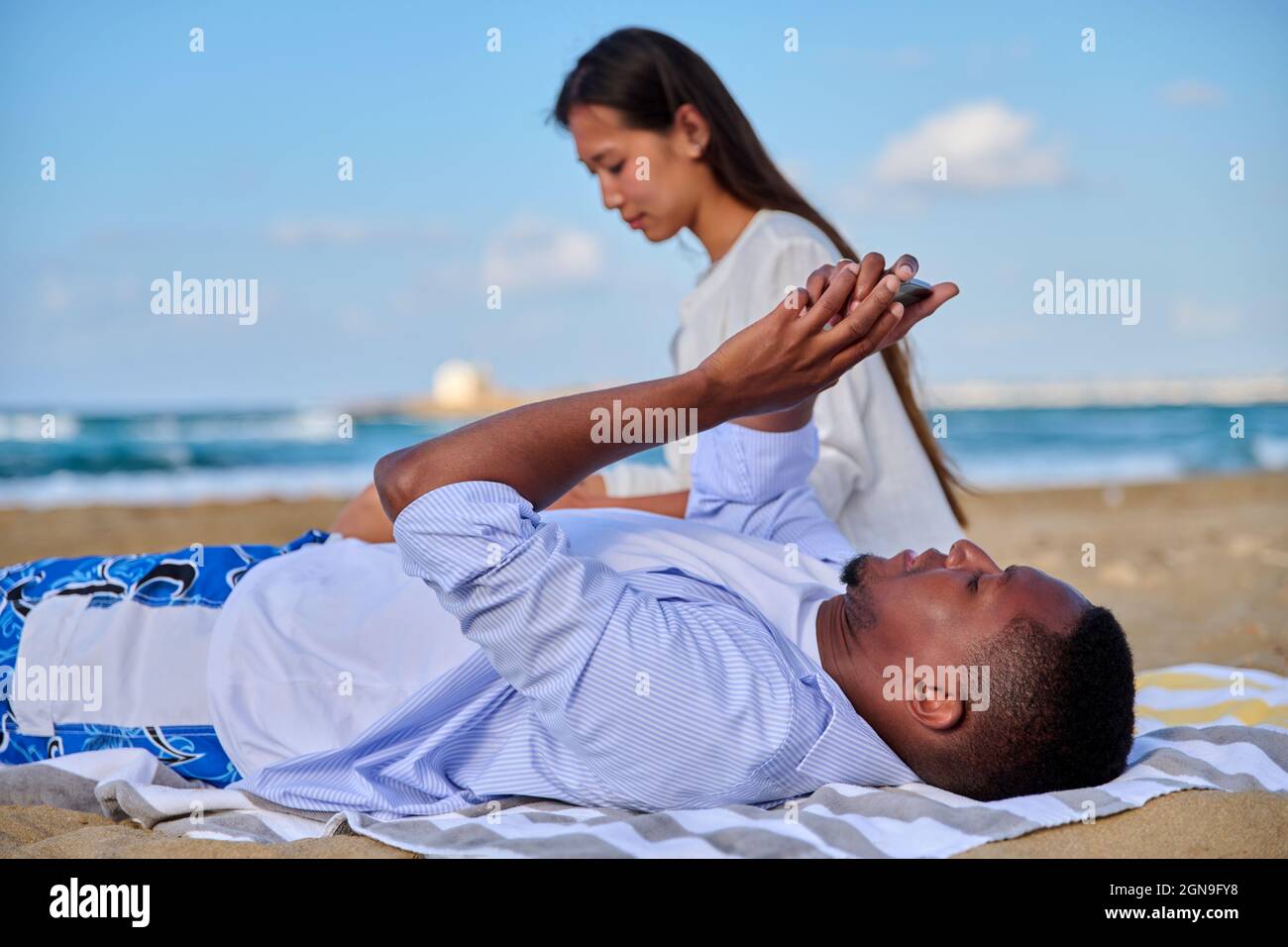 Young beautiful couple having a rest on the beach, man with smartphone Stock Photo