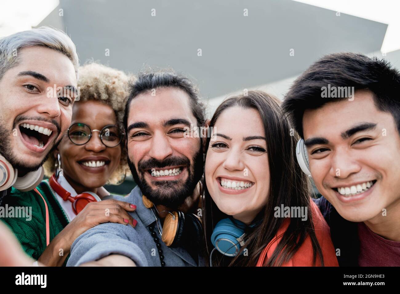 Multiracial friends having fun taking a group selfie portrait with mobile phone outdoor in the city - Focus on center girl face Stock Photo