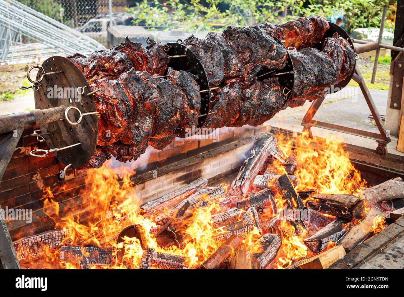 Eight hundred pounds of beef skewered on a custom made motor driven spit barbecue on an open flame fire pit.  Festival barbecue stand. Stock Photo
