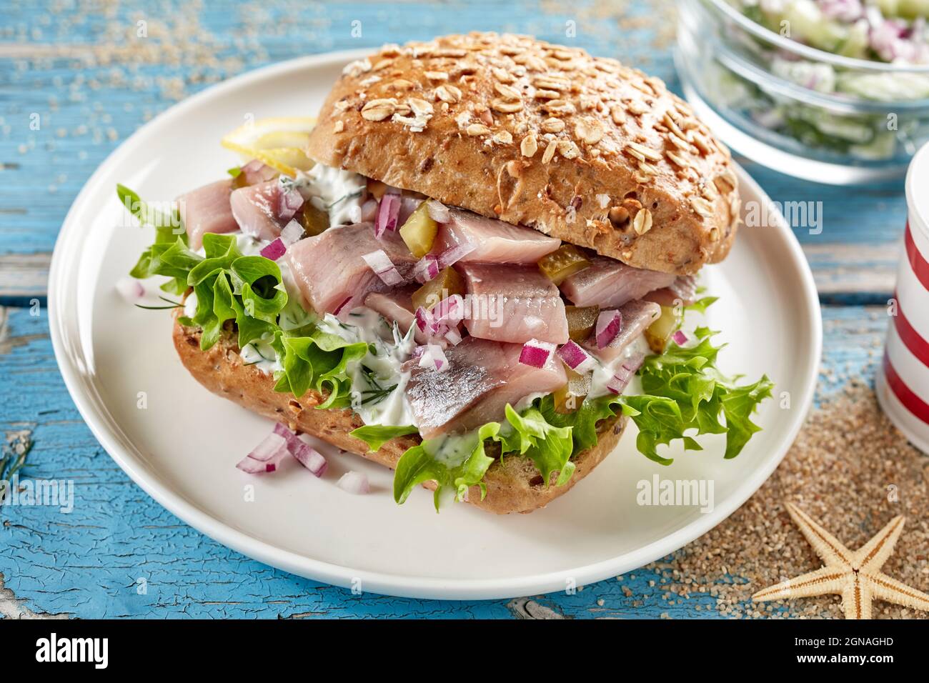 From above of nutritious sandwich bun with herring and pickles served on plate on wooden table decorated in marine style Stock Photo