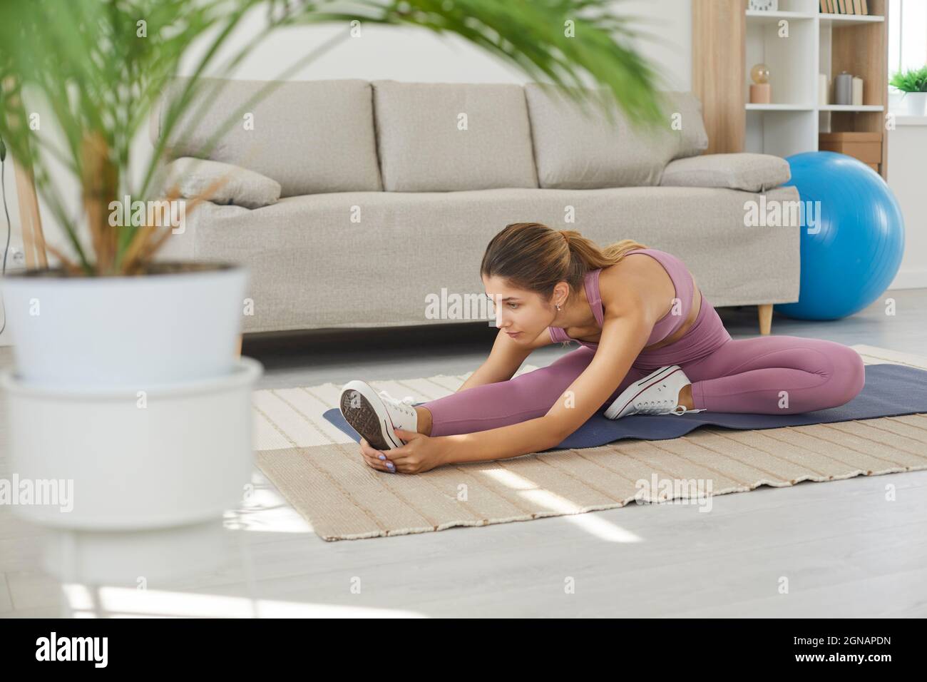 Fit young woman doing leg stretching exercise during her fitness workout at home Stock Photo