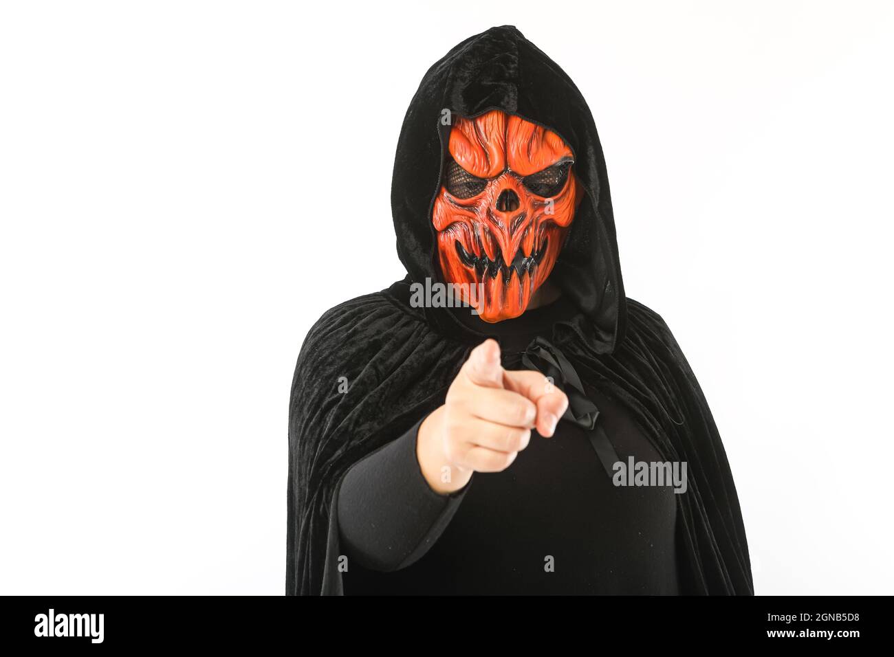 Person dressed in pumpkin latex mask and velvet cloak with hood, pointing with hand, on white background. Carnival, Halloween and days of the dead con Stock Photo