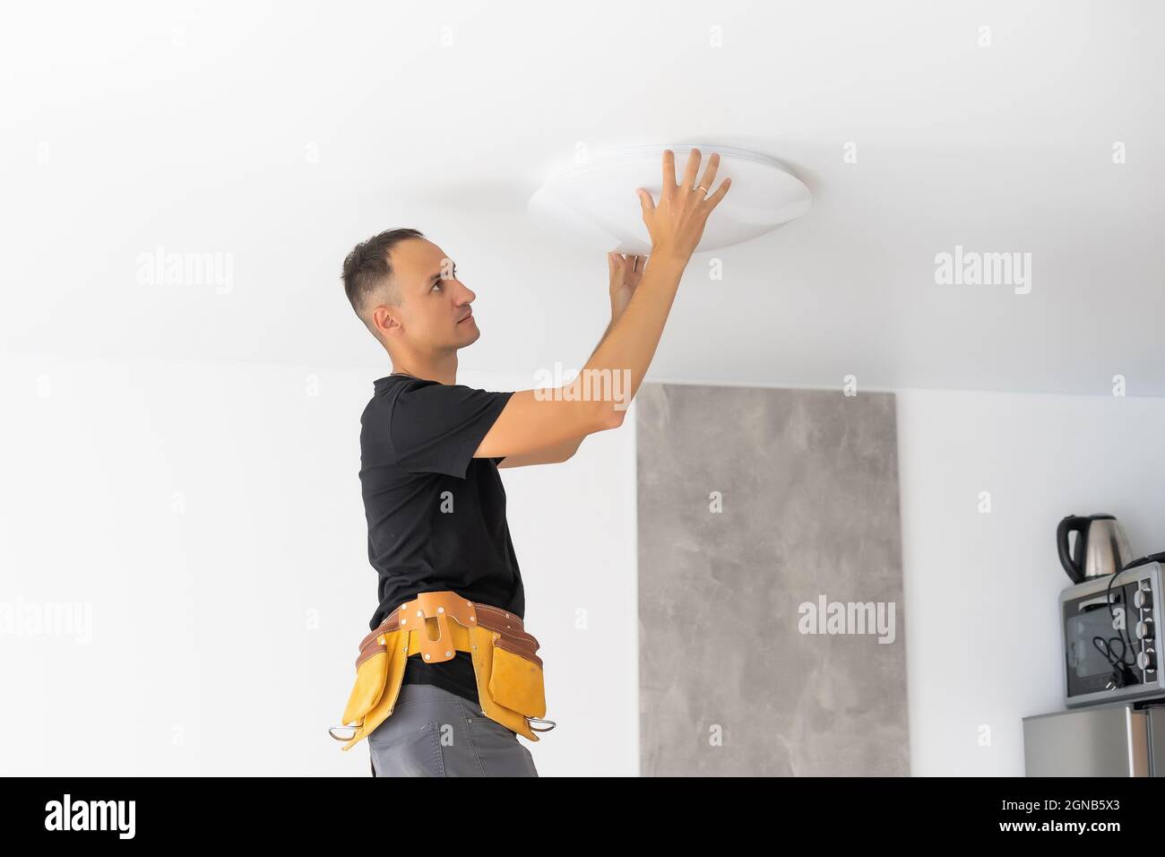 Worker repairing lamp on stretch ceiling indoors Stock Photo