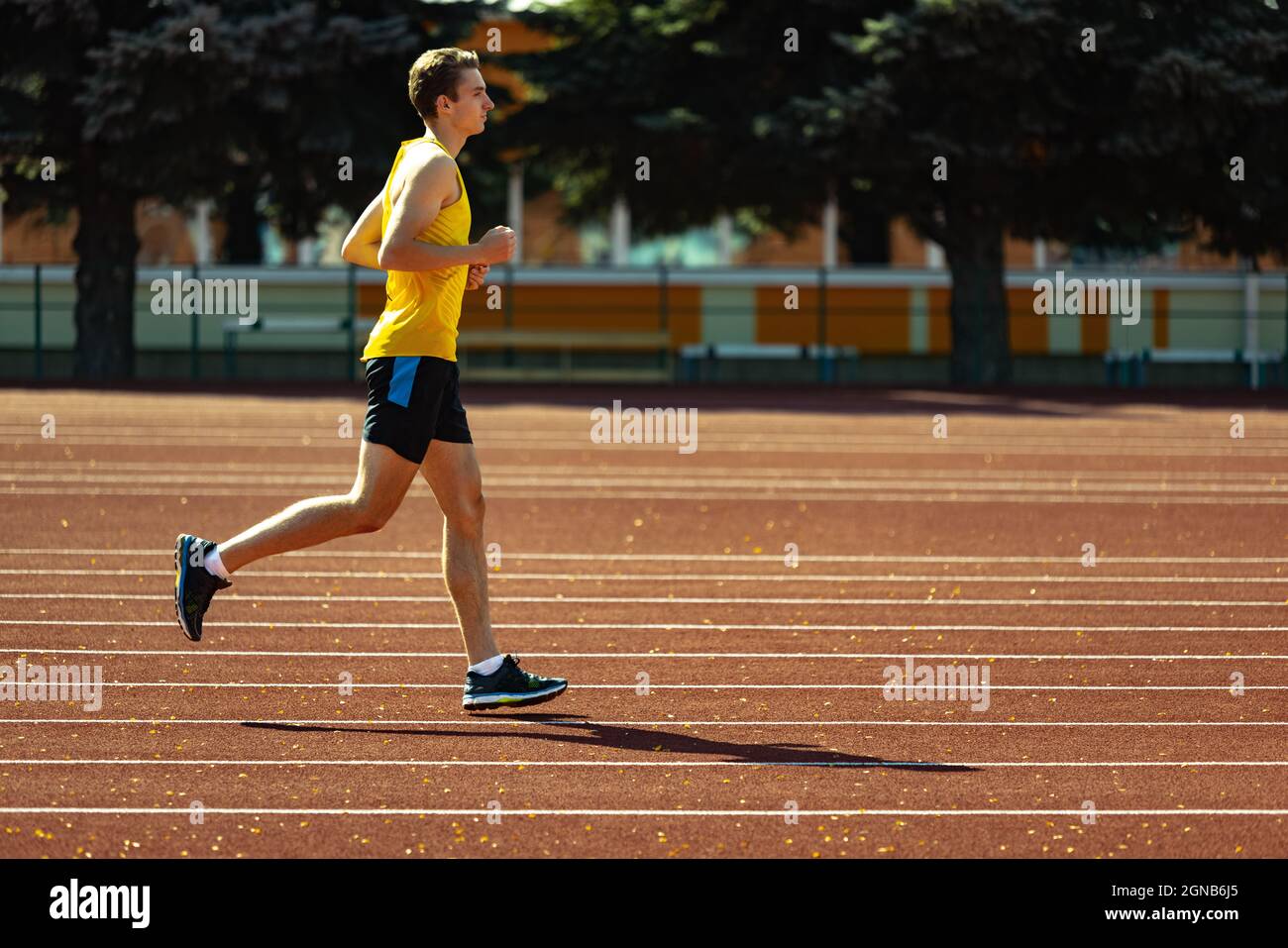 Young Caucasian sportive man, male athlete, runner jogging at public stadium, sport court or running track outdoors. Summer sport games. Stock Photo