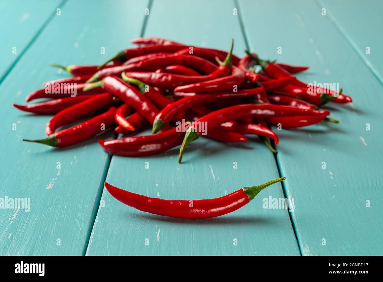 https://c8.alamy.com/comp/2GNBD17/red-hot-chili-pepper-pod-in-front-of-raw-chilli-peppers-pile-over-turquoise-wooden-table-whole-fresh-pungent-chiles-for-cooking-spicy-dishes-2GNBD17.jpg
