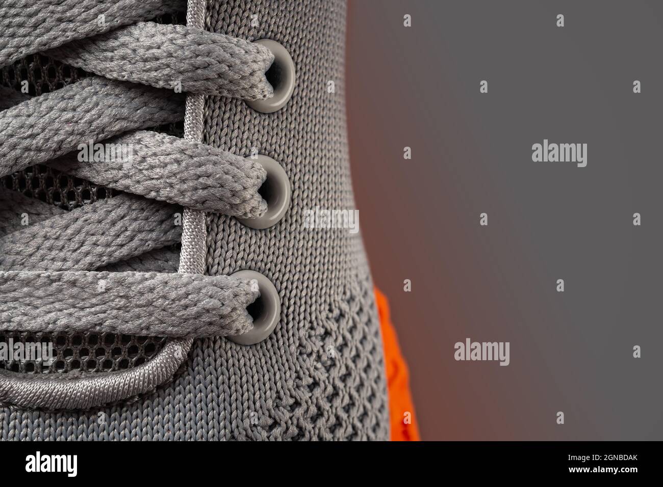 Laced up gray mesh fabric sneakers macro shot. Lace fastening of new orange sole sport shoe close-up. Modern textile shoes elastic laces. Copy space. Stock Photo