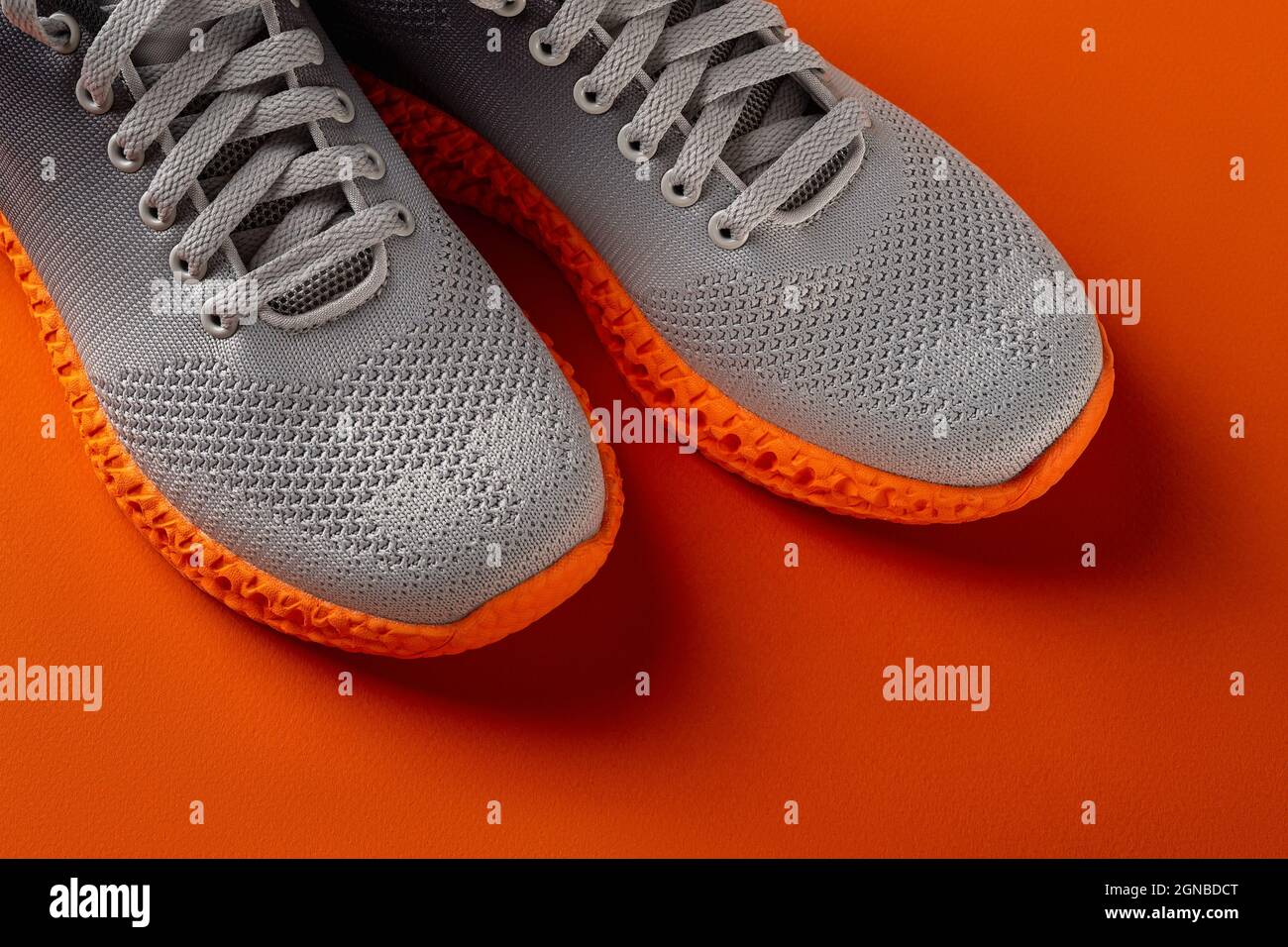Pair of grooved orange sole sneakers from gray mesh fabric over orange background. Laced up stylish  textile trainers for active lifestyle, fitness. Stock Photo