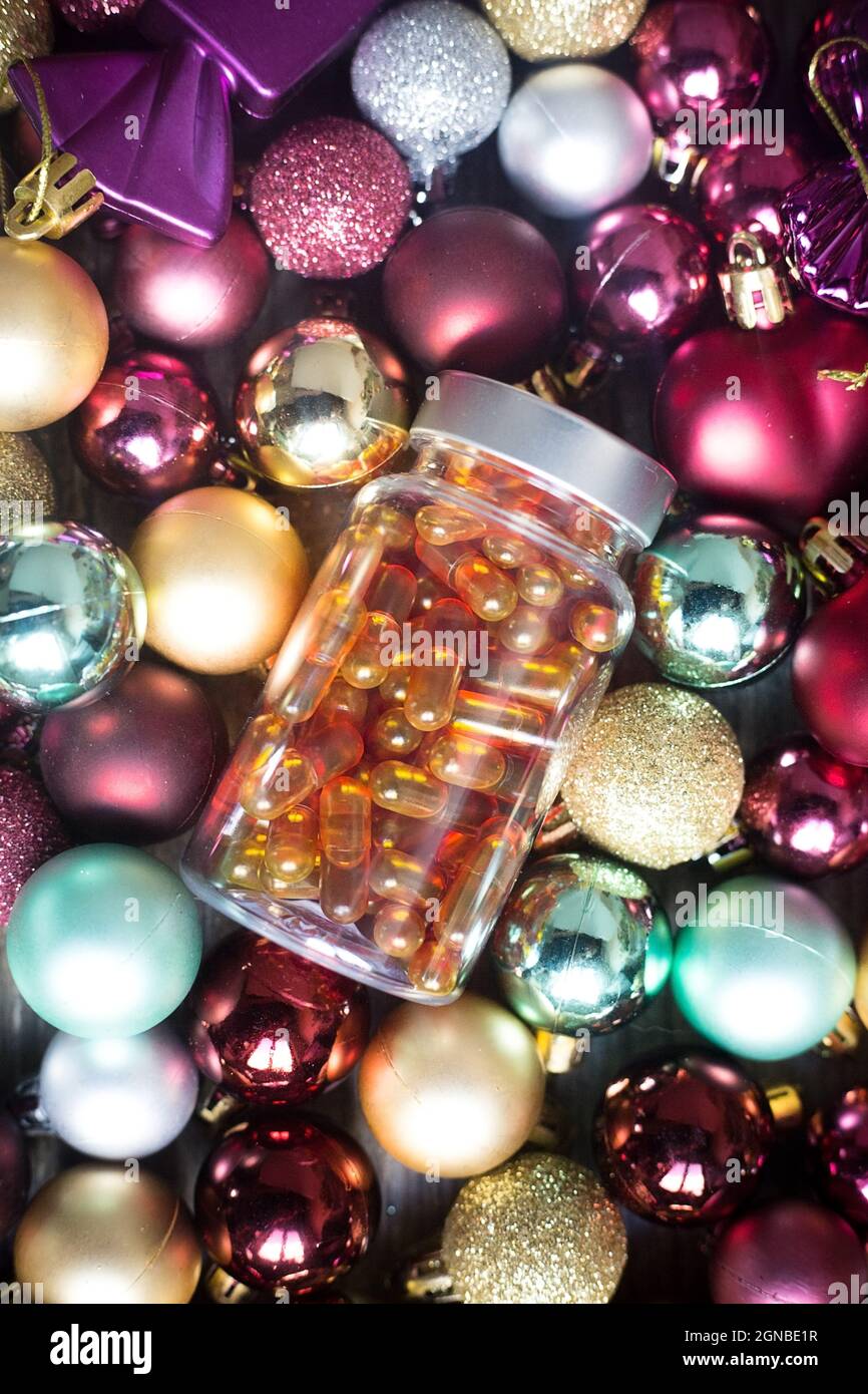 Vertical picture. Plastic bottle with orange pills. Fish fat and vitamin D capsules on Christmas balls. Coronavirus prevention. Healthy new year. Best Stock Photo