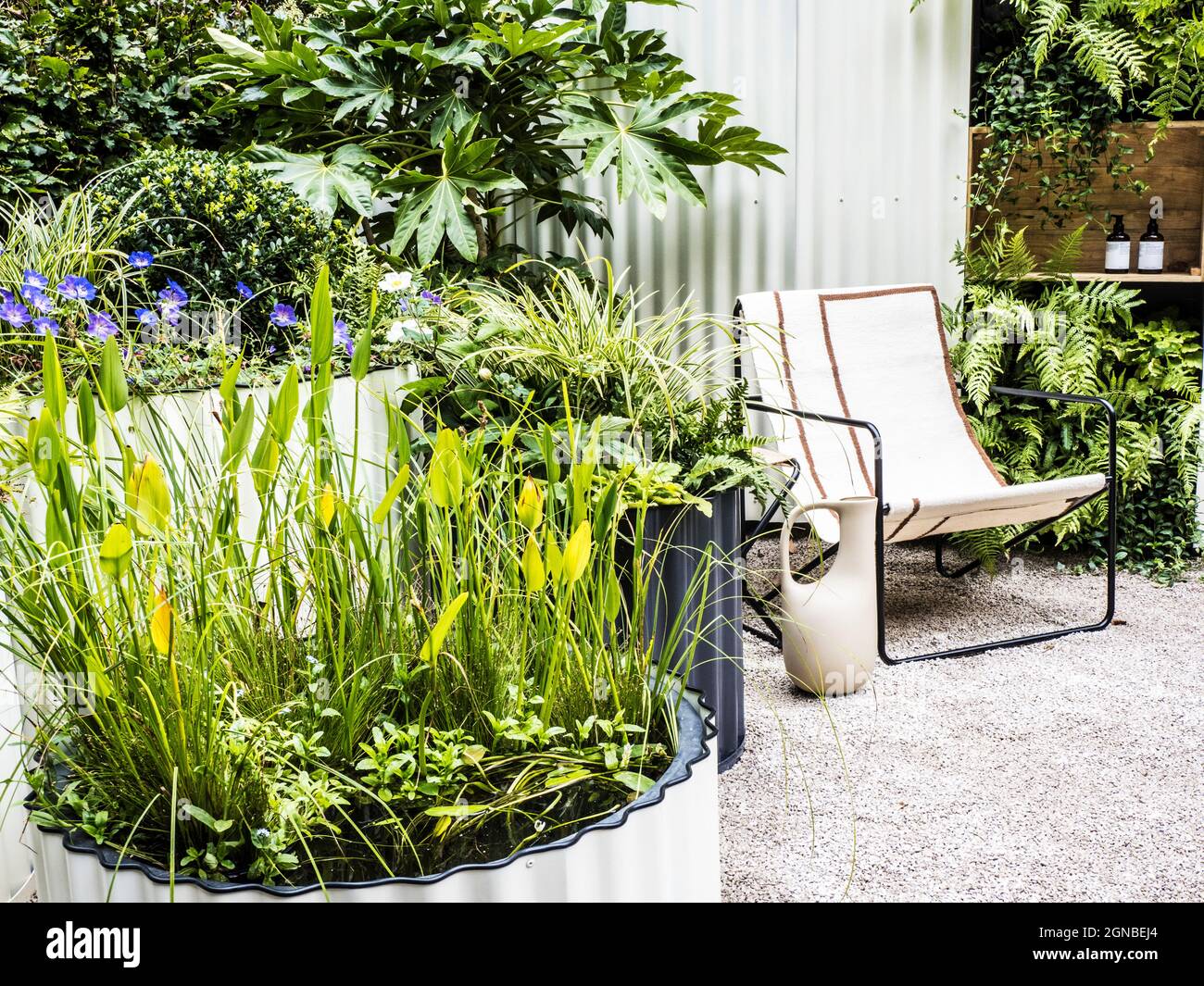 A gravel patio with chair and richly planted containers. Stock Photo