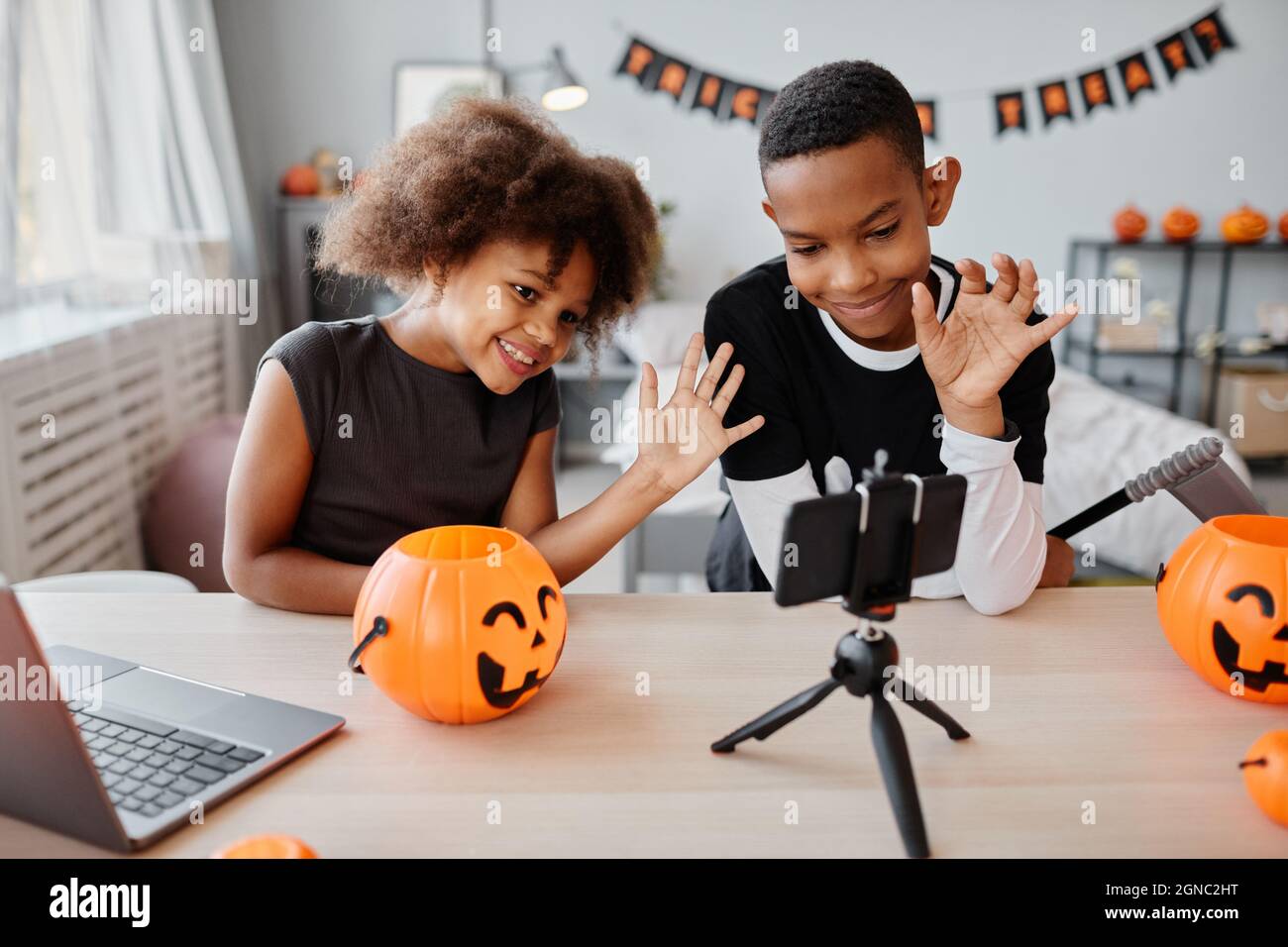 Two smiling African-American kids waving at smartphone while video chatting on live streaming on Halloween Stock Photo