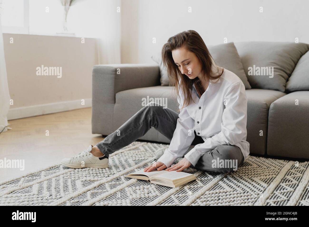 Young woman sitting on the floor at home and reading book. Stock Photo