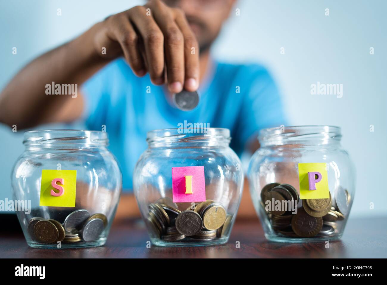 Focus on jar, Man from behind placing coins inside the jar - Concept of monthly SIP or systematic investment plan Stock Photo
