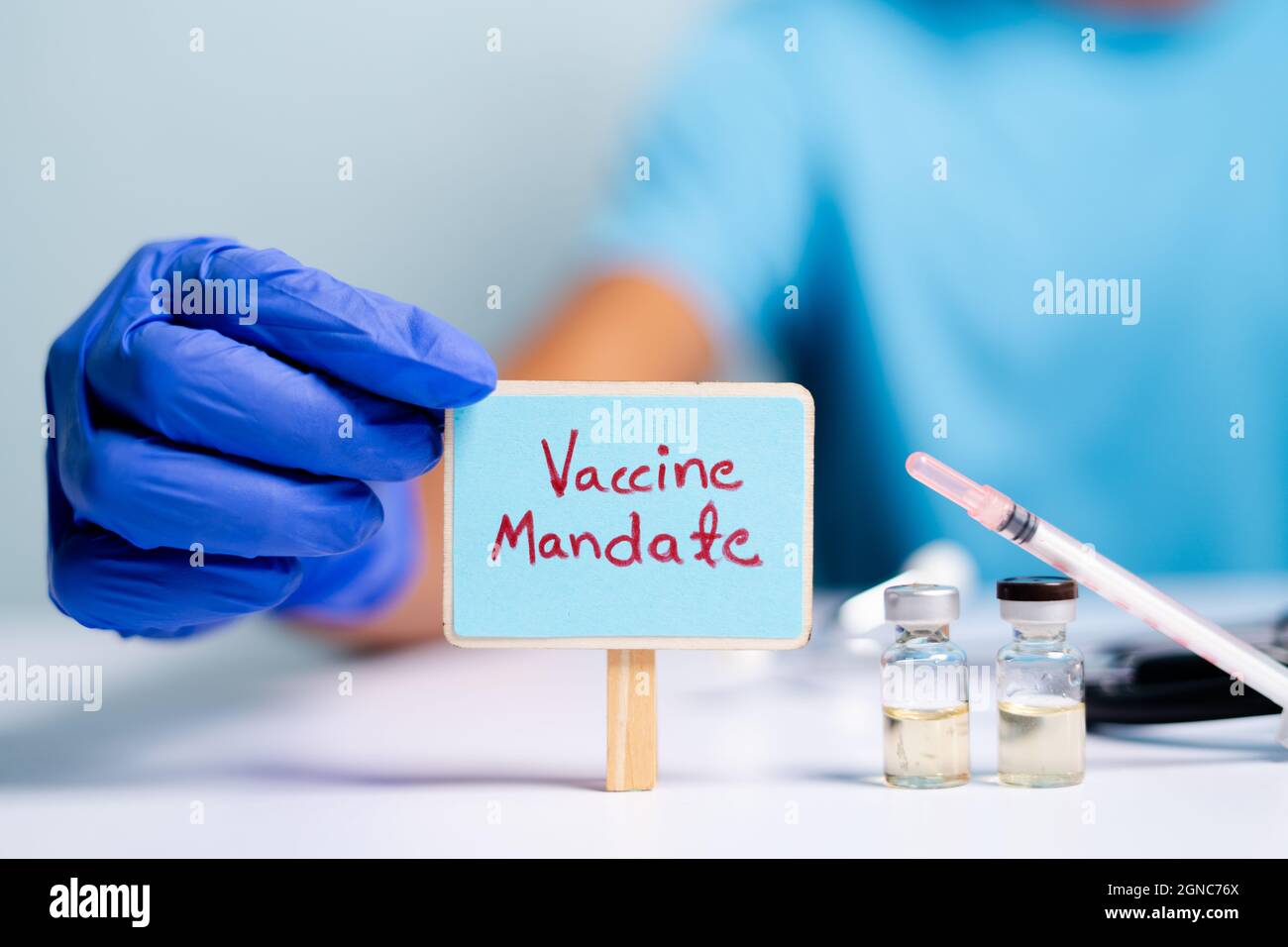 Concept of coronavirus or covid-19 vaccine mandate, showing with doctor hands with gloves by placing sign board next to vaccine shots and syringe Stock Photo