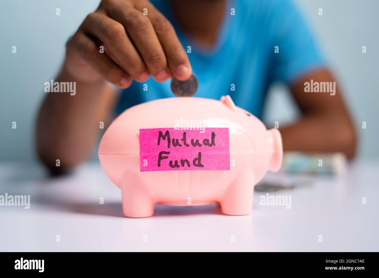 Concept of mutual fund investment, showing with hands placing coins inside the piggy bank with mutual fund sticker Stock Photo