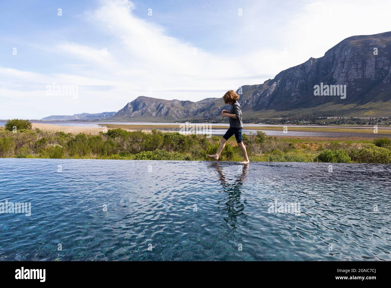 Eight year old boy walking around the edge of an infinity pool, a mountain backdrop Stock Photo