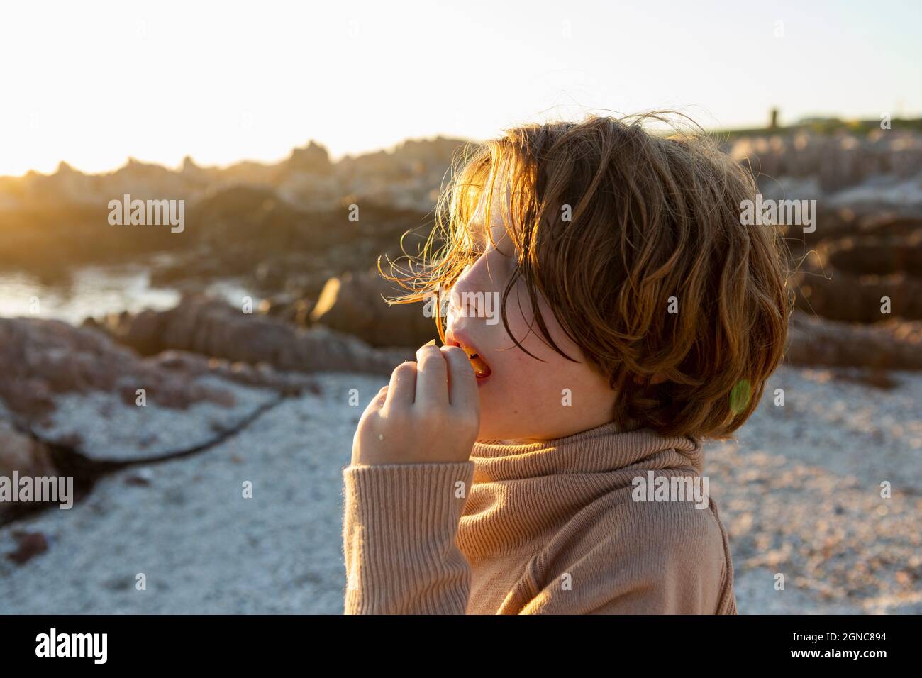 A boy on the beach at sunset, having a snack. Stock Photo