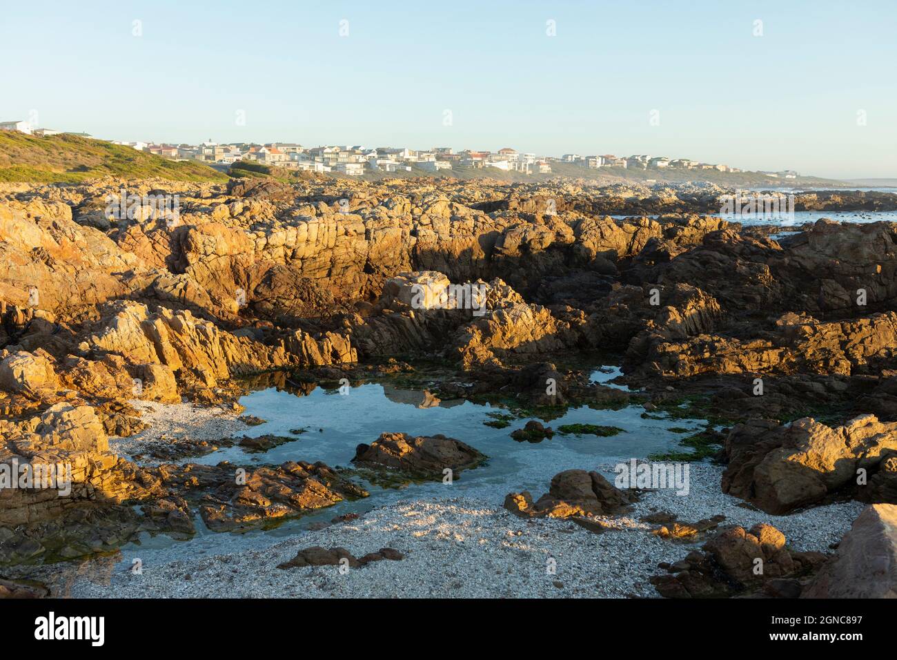 Jagged rocks and rock pools on the Atlantic Ocean coastline and houses on the headland. Stock Photo