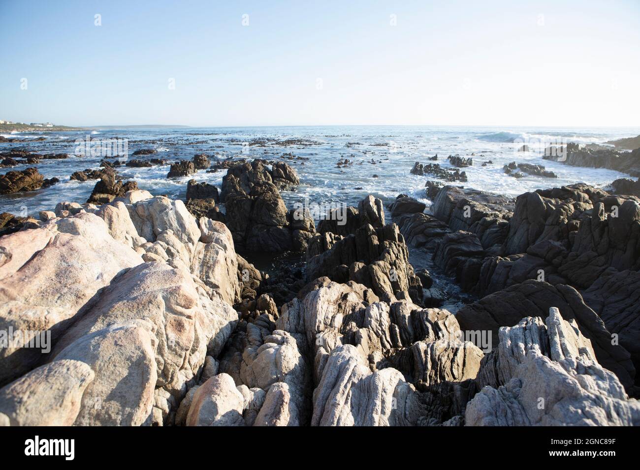 Jagged rocks ridges leading out into the sea, and waves breaking on shore at De Kelders Stock Photo