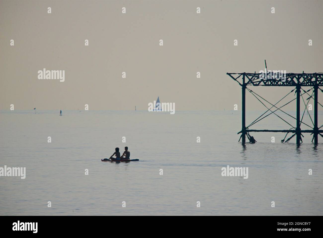 The dilapidated West Pier, Brighton. East Sussex, England. Looking east from Hove.  East Sussex, England. Two paddleboarder ssilhouetted against the skeletal rusting structure of the old pier. Stock Photo