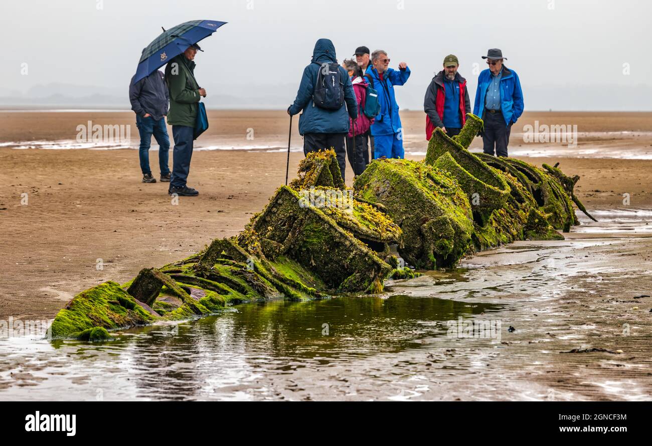 Group of walkers looking at decayed historic wreck of World War II XT class midget submarine buried in sand, Aberlady Bay, East Lothian, Scotland, UK Stock Photo