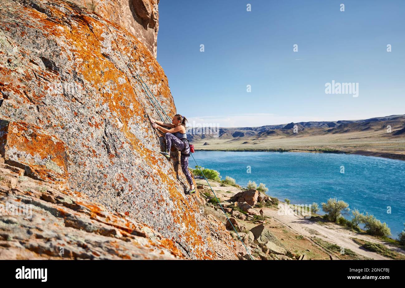 Young athlete woman is climbing on the high rock at sunset near Ili River in Kazakhstan Stock Photo