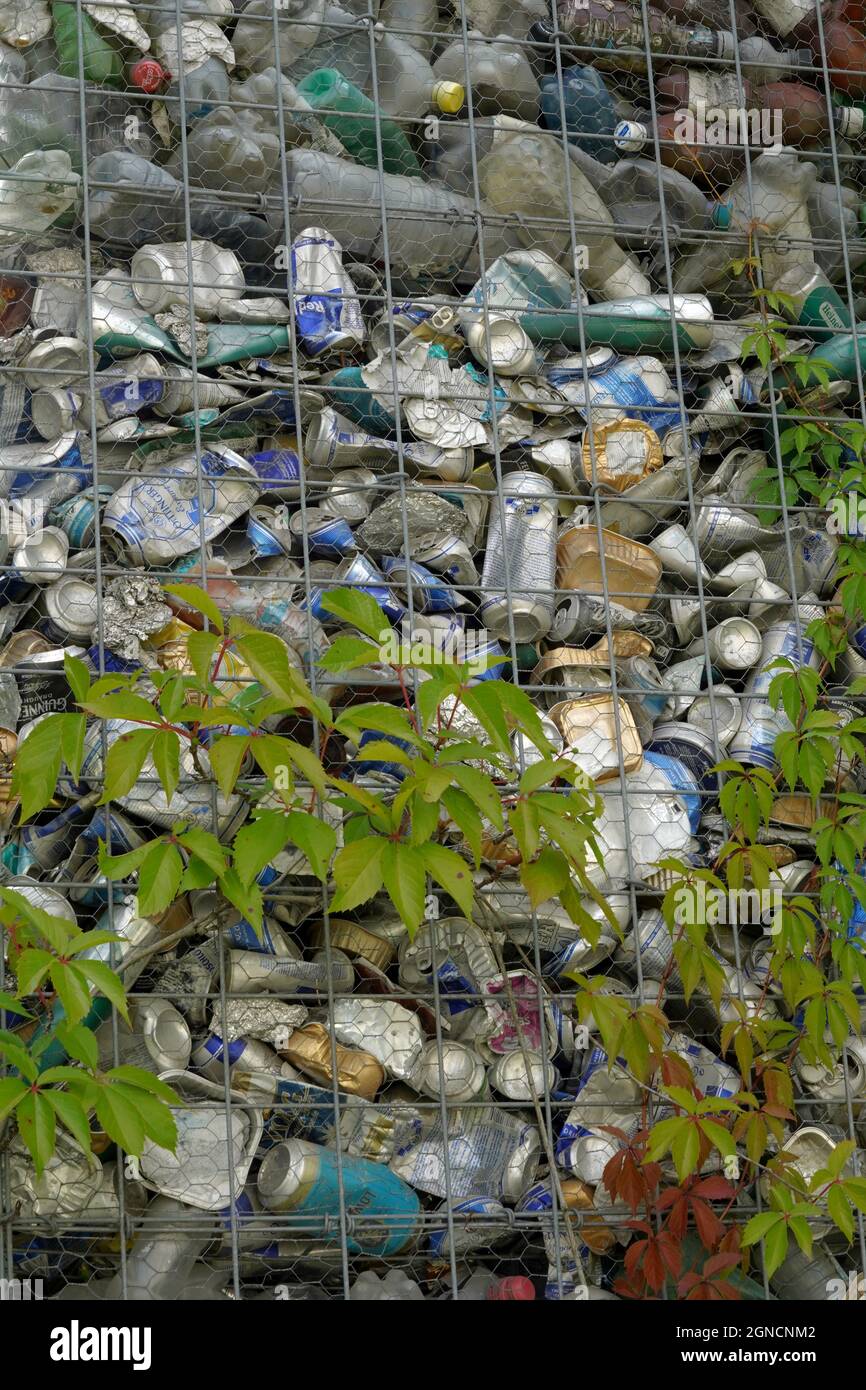 Detail of plastic bottles and aluminium cans squashed and compressed. They are put in a metal structure for fence. There are creeping plants growing. Stock Photo