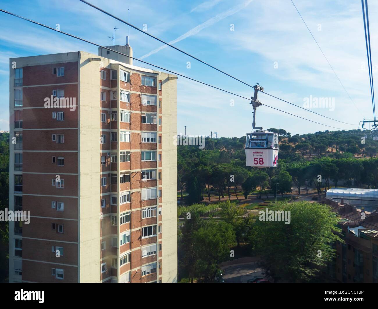 Cable car cabins circling above Madrid's Casa de Campo between trees and buildings. Stock Photo