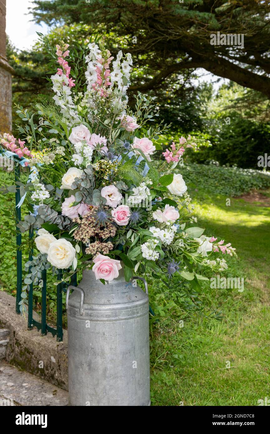 Close up of a flower arrangement in a milk churn outside a church on a