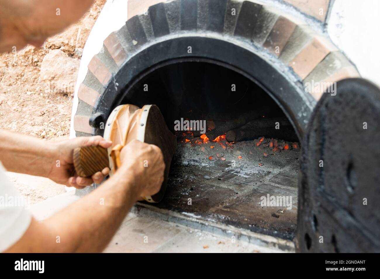 Artisan woodfired oven and man's hands blowing the embers with a