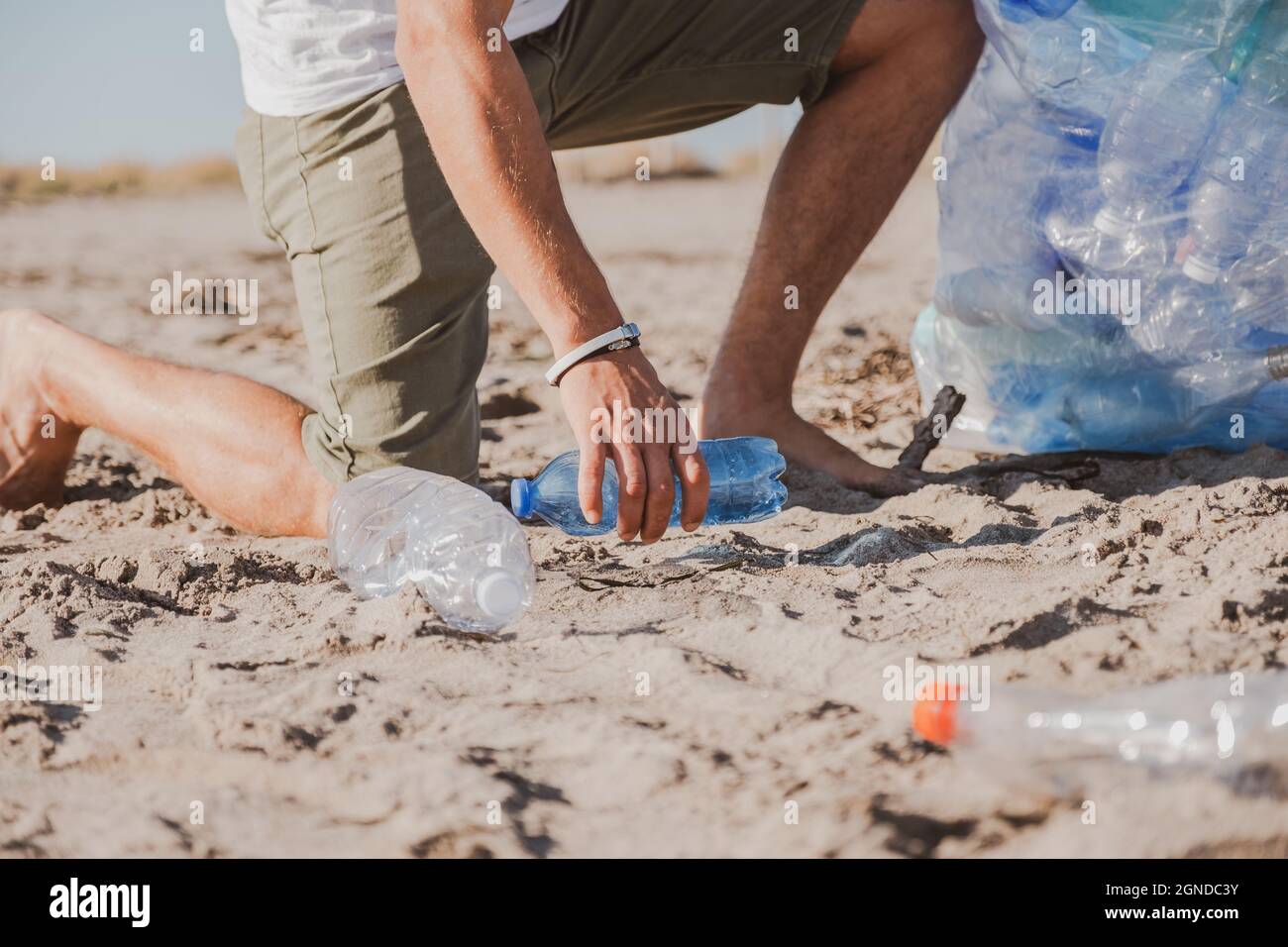 Young man gathering a plastic bottle and cleaning the beach Volunteer concept. Plastic free. We have not planet b. Save earth from plastic Stock Photo