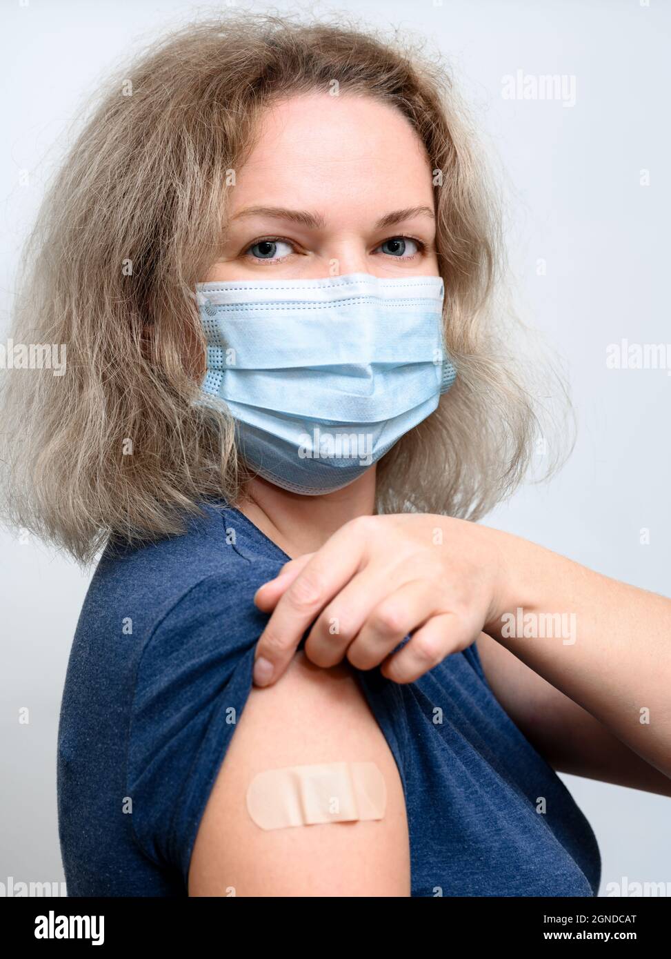 Person after getting COVID-19 vaccine, portrait of pretty woman in medical mask showing arm with plaster. Concept of people coronavirus vaccination, v Stock Photo