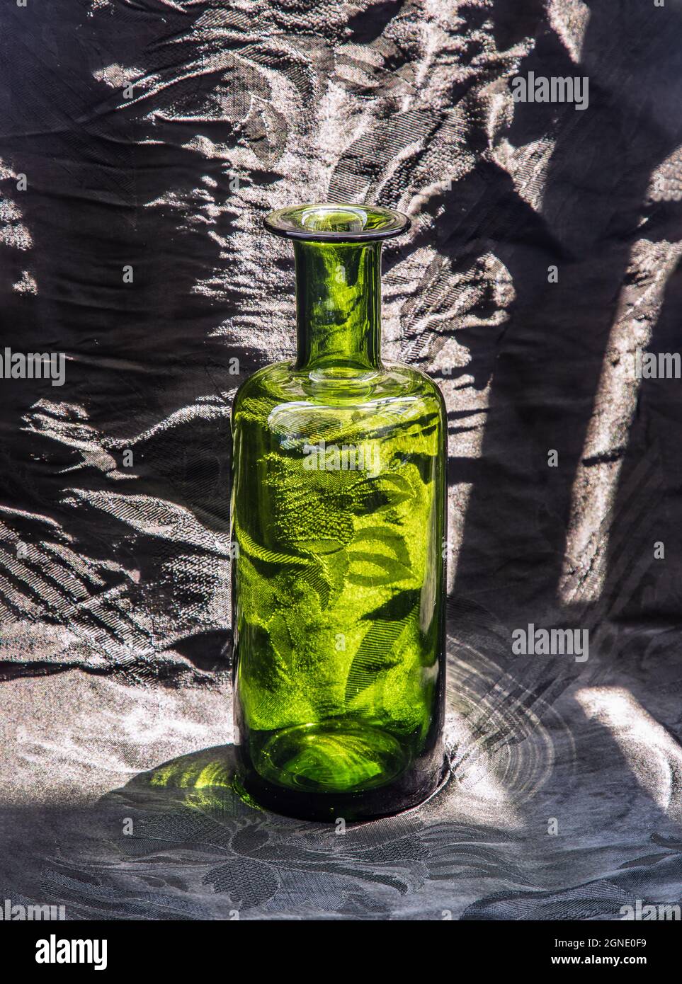A green glass bottle and surface reflections on a black background ...