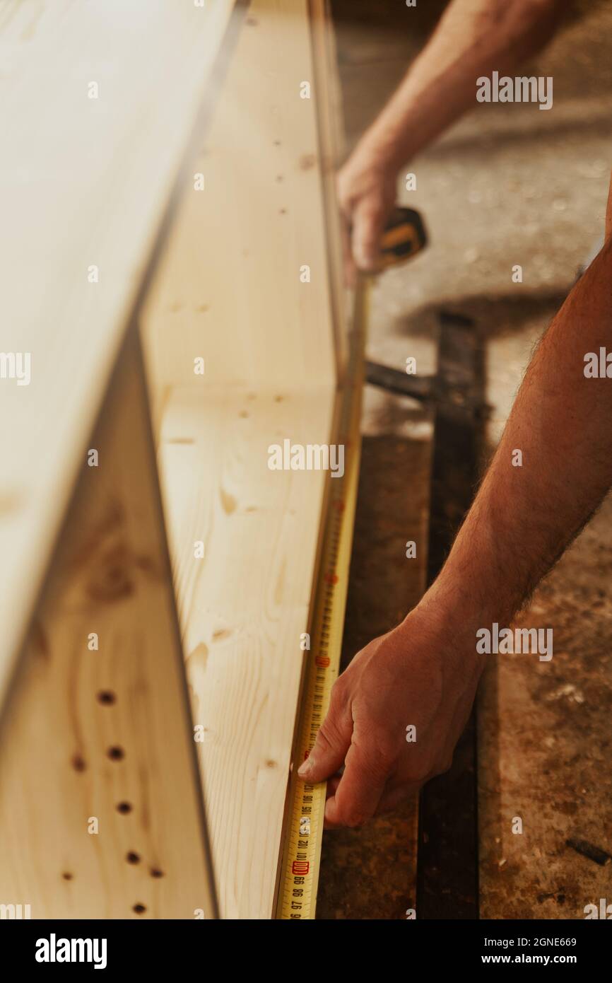 Carpenter taking measurements of an unfinished cabinet in a woodworking factory or workshop using a handheld tape measure Stock Photo