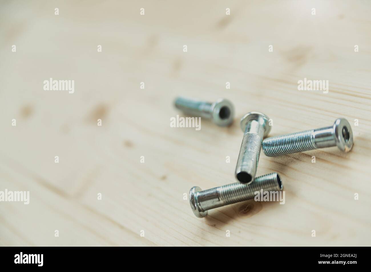 Four threaded steel screws lying on a workbench or plank if timber in a