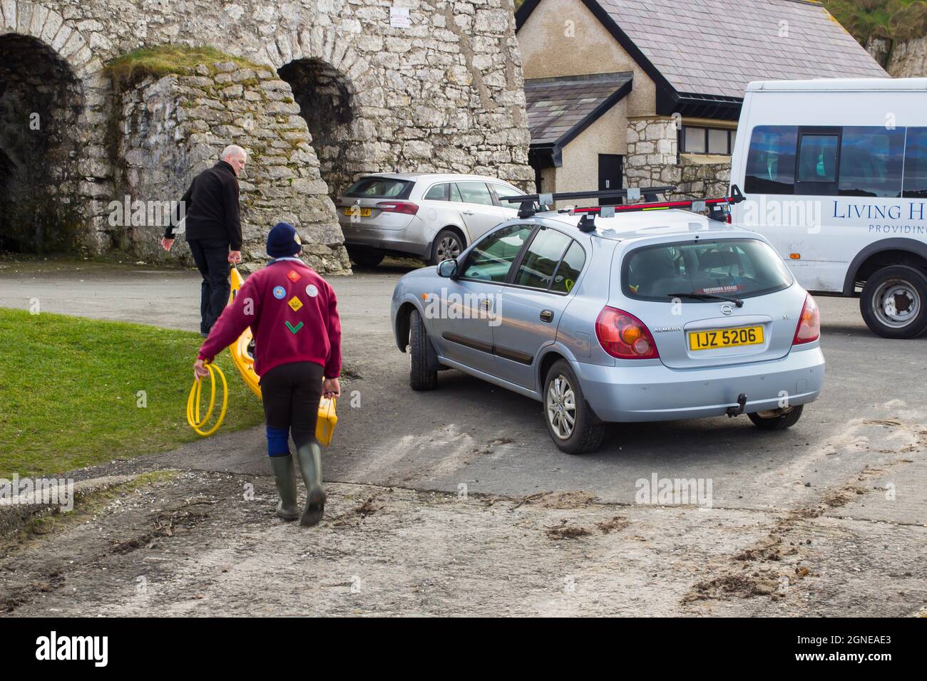 11 March 2017 A pair of male youth leaders unloading a small canoe from a car roof rack on a dull spring afternoon in Ballintoy harbour on the Atlanti Stock Photo