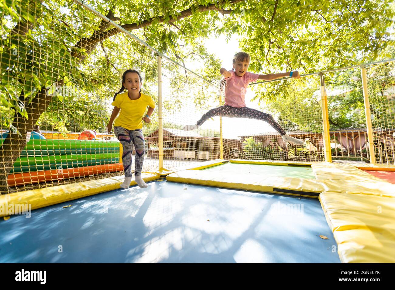 Little pretty girls having fun outdoor. Jumping on trampoline in children  zone. Amusement park Stock Photo - Alamy
