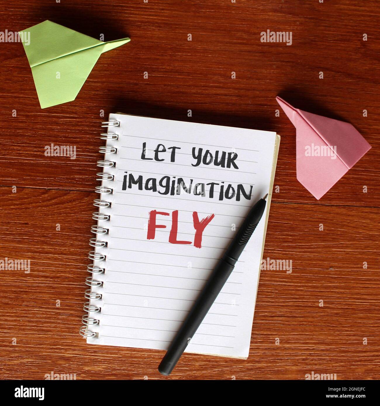 Motivational and inspirational quotes. Top view image of paper plane and notebook with text LET YOUR IMAGINATION FLY Stock Photo