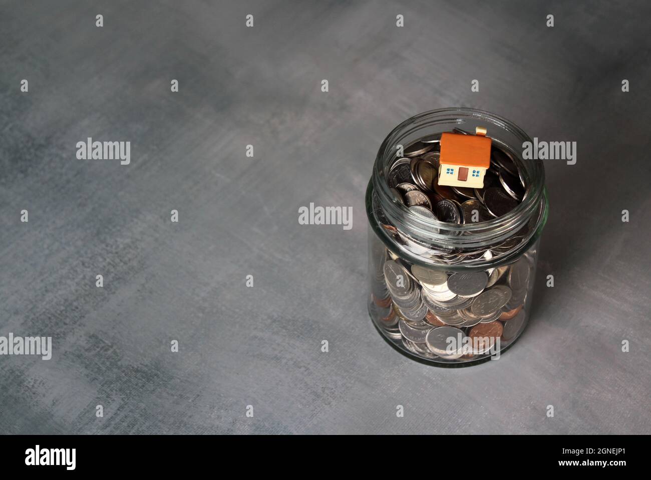 Real estate, property and financial concept. Close up image of coins in glass jar with miniature house. Copy space for text Stock Photo
